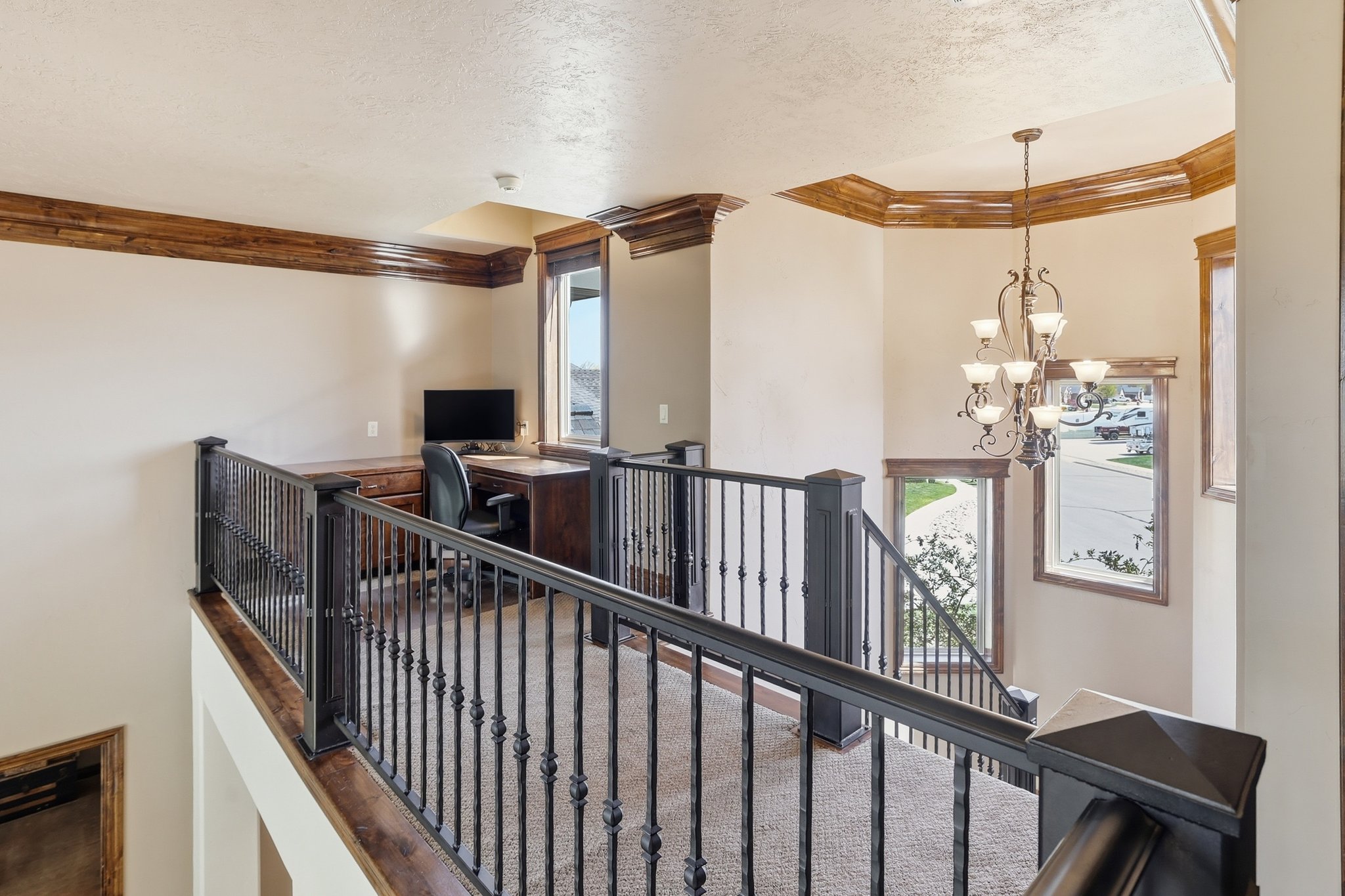 Upper-level landing featuring a built-in wood-finish desk, iron baluster railing, and a multi-arm chandelier