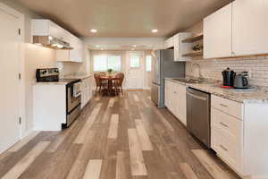Kitchen featuring white cabinets, stainless steel appliances, open shelves, light wood-style flooring, and decorative backsplash