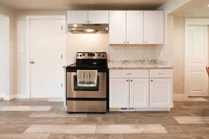 Kitchen with electric stove, white cabinetry, light wood finished floors, light stone counters, and tasteful backsplash