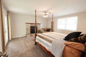 Bedroom featuring carpet flooring, a ceiling fan, and a stone fireplace