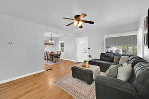 Living room with light wood-type flooring, ceiling fan, and suspended lighting