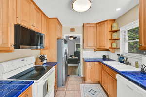 Kitchen featuring tile countertops, white appliances, open shelves, and tasteful backsplash