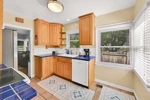 Kitchen featuring open shelves, white dishwasher, tile counters, freestanding refrigerator, and light tile patterned flooring