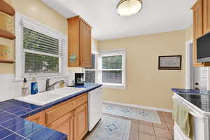 Kitchen with tile countertops, electric range, white dishwasher, open shelves, and light tile patterned floors