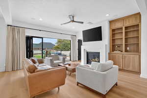 Living room with a ceiling fan, a glass covered fireplace, light wood-type flooring, a textured ceiling, and recessed lighting