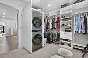 Laundry area with arched walkways, stacked washer / dryer, recessed lighting, and light carpet