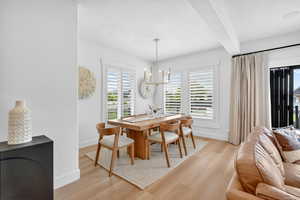 Dining room featuring light wood-style flooring, hanging lights, a textured ceiling, and beam ceiling
