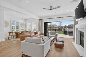 Living room with a fireplace with flush hearth, ceiling fan, light wood finished floors, and suspended lighting