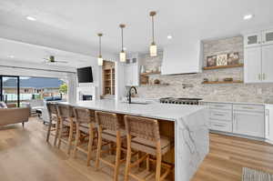 Kitchen with glass fronted cabinets, light stone counters, white cabinetry, light wood-type flooring, and a textured ceiling