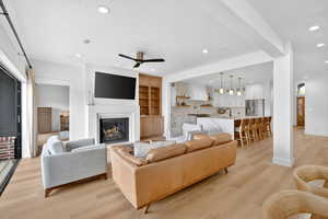 Living area with light wood-style floors, a glass covered fireplace, ceiling fan, and recessed lighting