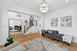 Living room with an office area, light wood-style flooring, and suspended lighting