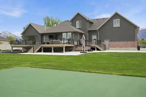 Back of property featuring a deck with mountain view, stucco siding, brick siding, and a lawn