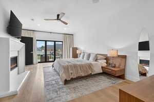 Bedroom featuring a glass covered fireplace, light wood finished floors, access to outside, ceiling fan, and a textured ceiling