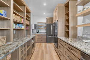 Kitchen with open shelves, light wood finished floors, stainless steel appliances, light stone countertops, and a textured ceiling