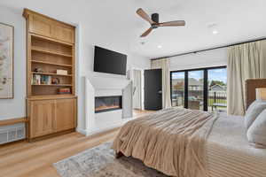 Bedroom with ceiling fan, access to outside, light wood finished floors, a glass covered fireplace, and recessed lighting