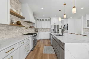 Two tone kitchen featuring glass insert cabinets, light stone countertops, stainless steel appliances, decorative backsplash, and light wood-type flooring