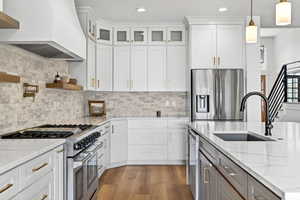 Kitchen with stainless steel appliances, dual tone cabinets, light stone countertops, light wood-style floors, and pendant lighting
