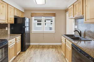 Kitchen featuring backsplash, light wood finish cabinetry, black appliances, and dark countertops