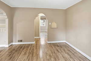 Empty room with light wood-type flooring, arched walkways, crown molding, and a textured ceiling