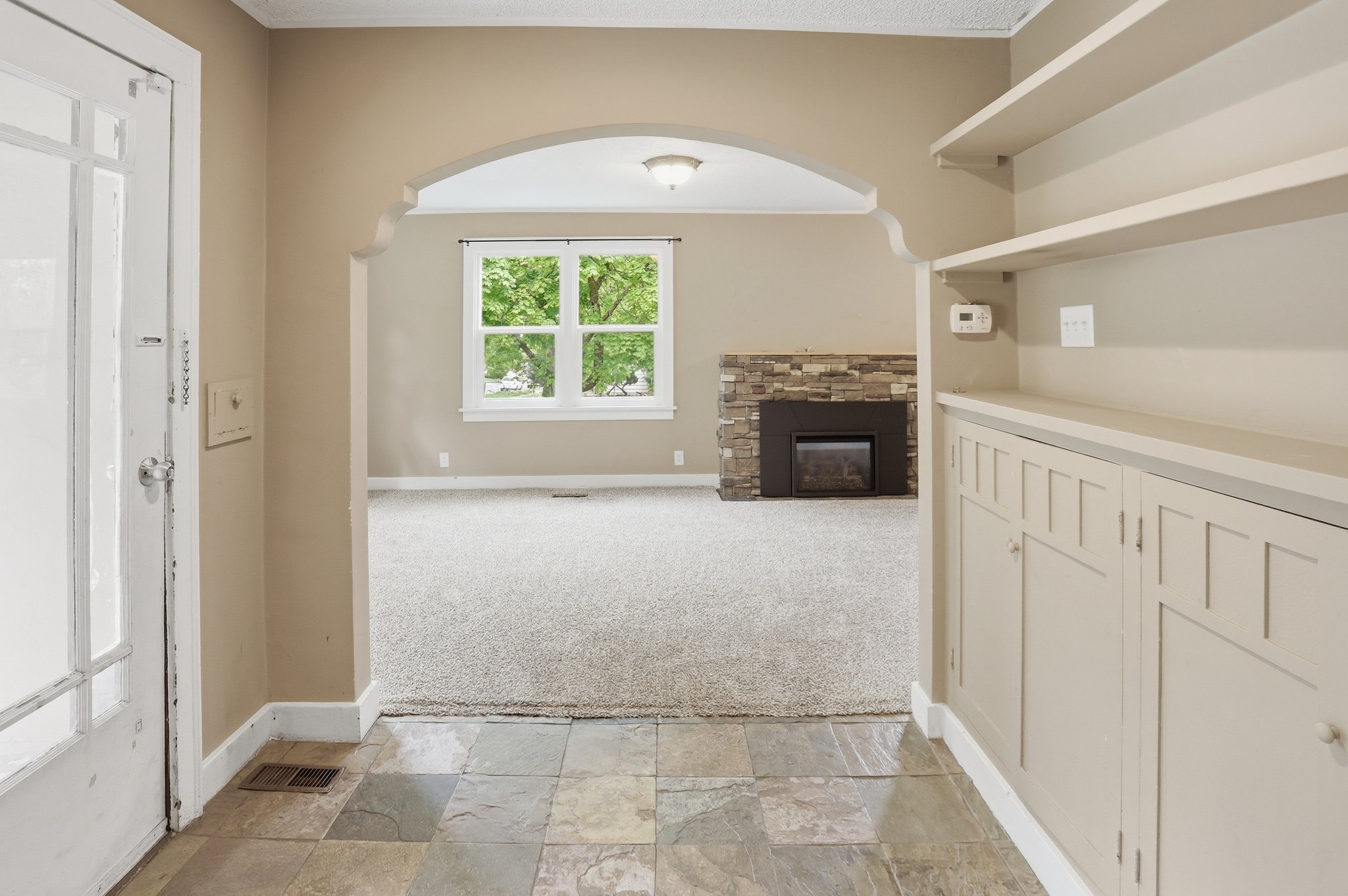 Unfurnished living room featuring stone tile floors, arched walkways, a fireplace, light colored carpet, and ornamental molding