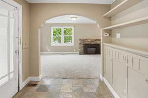 Unfurnished living room featuring stone tile floors, arched walkways, a fireplace, light colored carpet, and ornamental molding