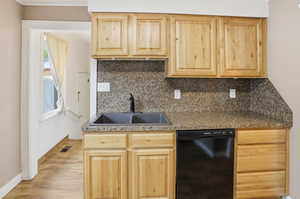 Kitchen with light wood finish cabinetry, black dishwasher, backsplash, and light wood-style floors