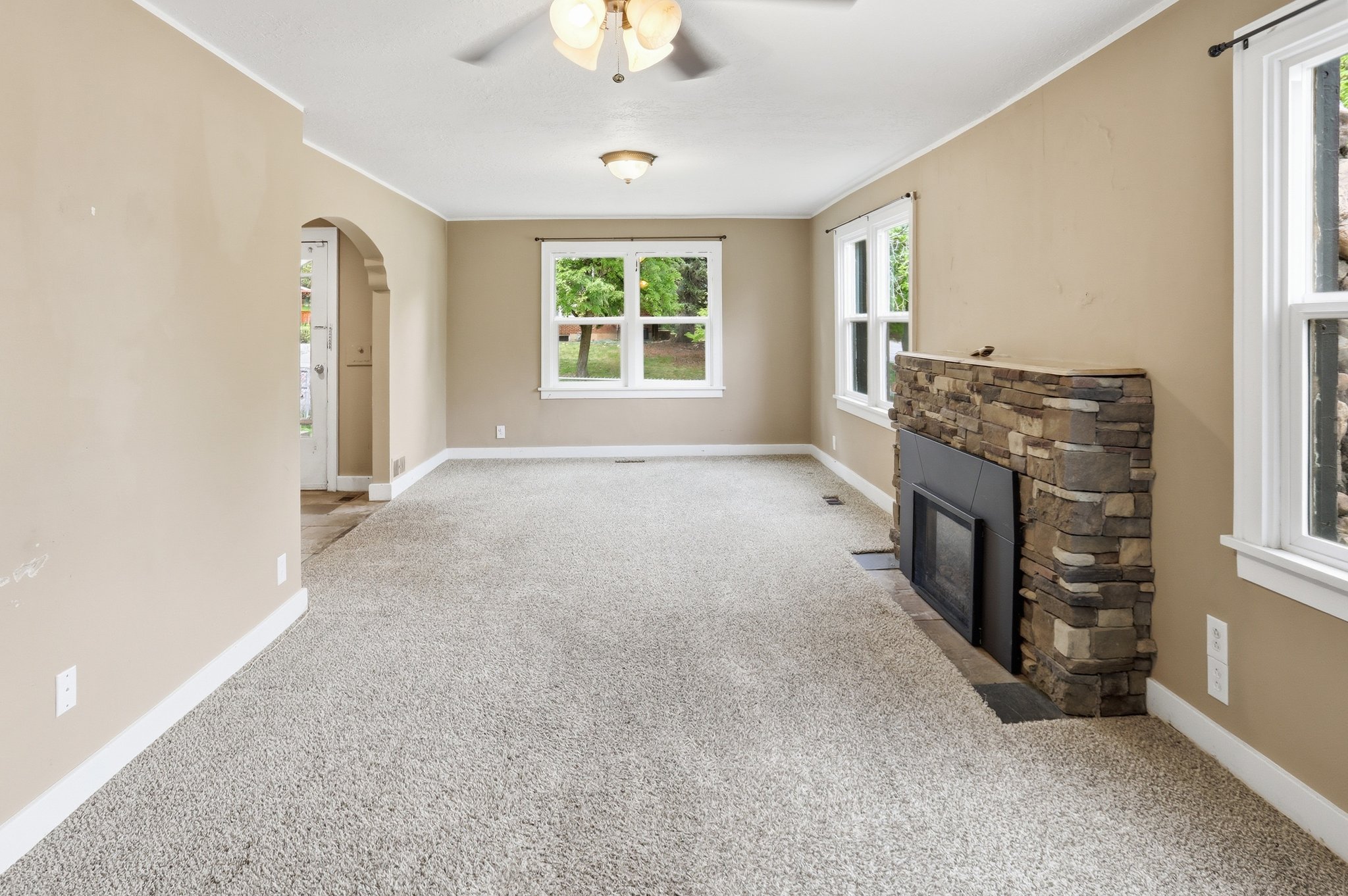 Unfurnished living room with arched walkways, light carpet, a fireplace, ornamental molding, and ceiling fan