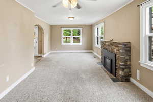 Unfurnished living room with arched walkways, light carpet, a fireplace, ornamental molding, and ceiling fan