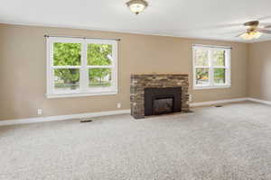 Unfurnished living room featuring ceiling fan, carpet floors, and a stone fireplace