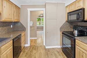 Kitchen featuring tasteful backsplash, black appliances, light wood finish cabinetry, light wood-style flooring, and ornamental molding