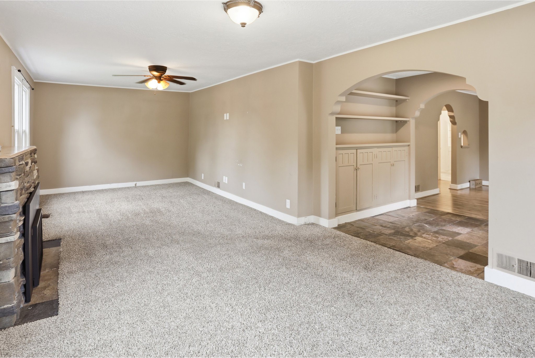 Unfurnished living room featuring ceiling fan, a fireplace, dark colored carpet, and arched walkways
