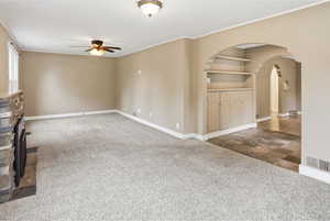Unfurnished living room featuring ceiling fan, a fireplace, dark colored carpet, and arched walkways