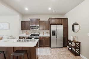 Kitchen featuring stainless steel appliances, dark wood finish cabinetry, light countertops, a breakfast bar, and recessed lighting