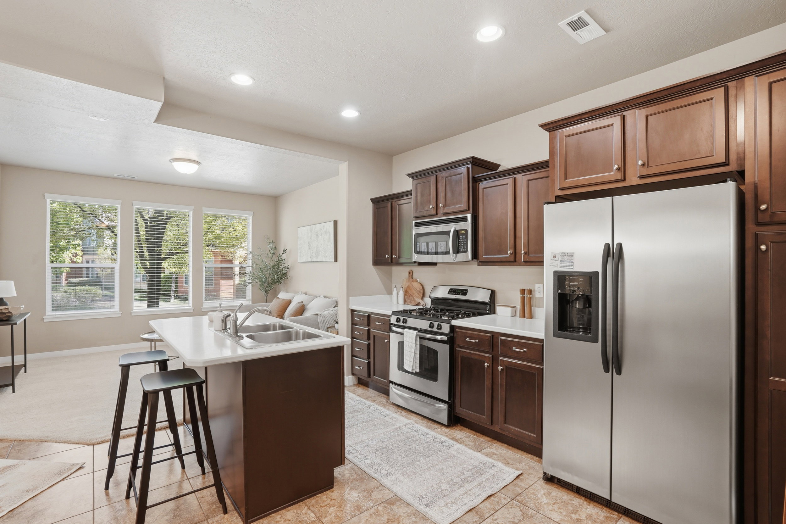 Kitchen with stainless steel appliances, light countertops, a center island with sink, a breakfast bar area, and dark wood finish cabinets