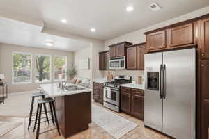 Kitchen with stainless steel appliances, light countertops, a center island with sink, a breakfast bar area, and dark wood finish cabinets