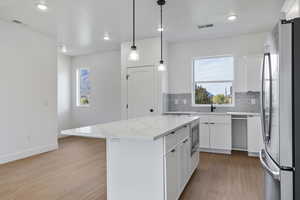 Kitchen with white cabinets, stainless steel appliances, light wood-style floors, light stone counters, and a kitchen island