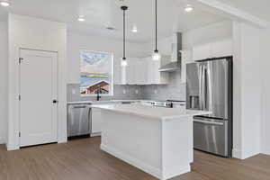 Kitchen featuring stainless steel appliances, white cabinetry, backsplash, a center island, and light wood-style floors