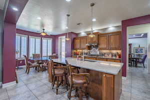 Kitchen with wood finish cabinets, light stone counters, hanging light fixtures, decorative backsplash, and a kitchen breakfast bar