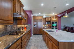 Kitchen featuring dark stone counters, stainless steel appliances, decorative light fixtures, and a kitchen island with sink