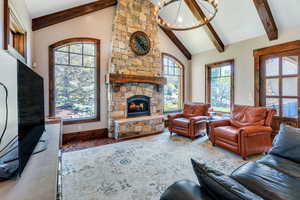 Living area with a stone fireplace, a chandelier, vaulted ceiling, wood finished floors, and plenty of natural light