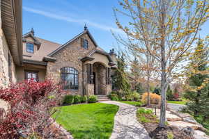 View of front of home featuring a front yard, a chimney, stucco siding, stone siding, and a shingled roof