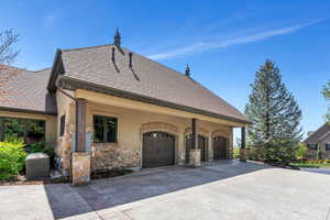 View of property exterior with driveway, stucco siding, stone siding, an attached garage, and roof with shingles