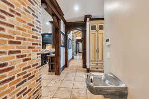 Corridor featuring arched walkways, decorative columns, recessed lighting, stone tile floors, and brick wall