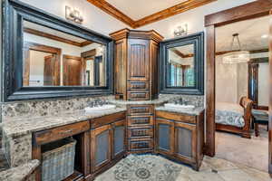 Bathroom featuring two vanities, connected bathroom, suspended lighting, ornamental molding, and light colored carpet