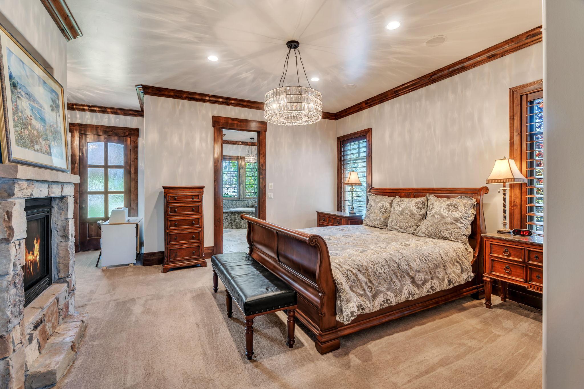Bedroom with light colored carpet, a stone fireplace, suspended lighting, and ornamental molding
