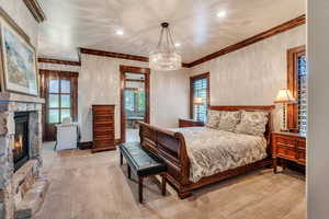 Bedroom with light colored carpet, a stone fireplace, suspended lighting, and ornamental molding