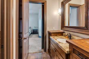 Ensuite bathroom featuring vanity, light stone finish floors, and light carpet