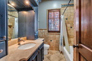 Full bath with vanity, shower / tub combo, tile walls, and wainscoting