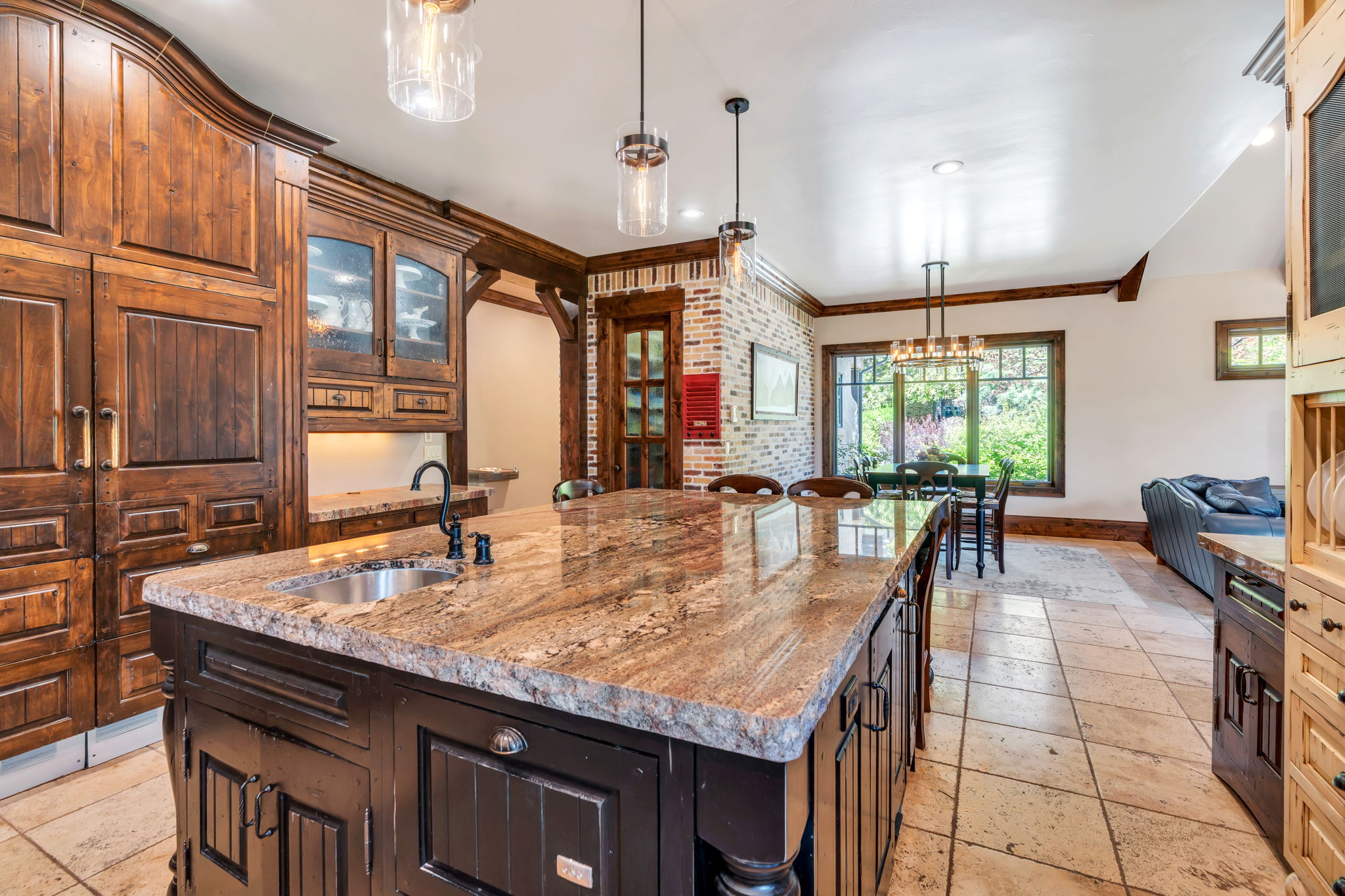 Kitchen featuring glass fronted cabinets, a center island with sink, ornamental molding, light stone counters, and stone tile flooring