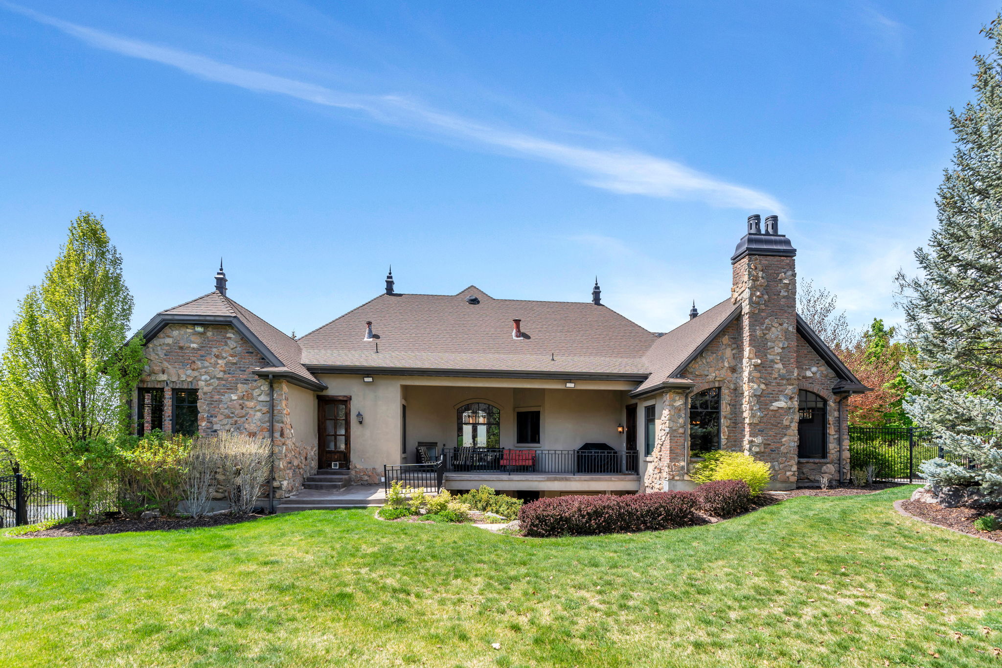 Back of house featuring stone siding, a chimney, stucco siding, a deck, and roof with shingles